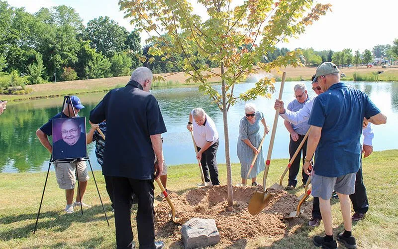 Several people use shovels to dig a hole and plant a tree.