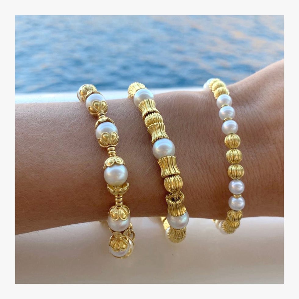 Three gold and pearl bracelets on a wrist.