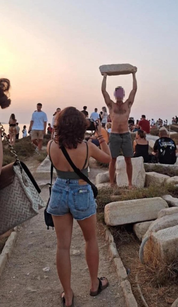 Tourist lifting rock while woman snaps photo.