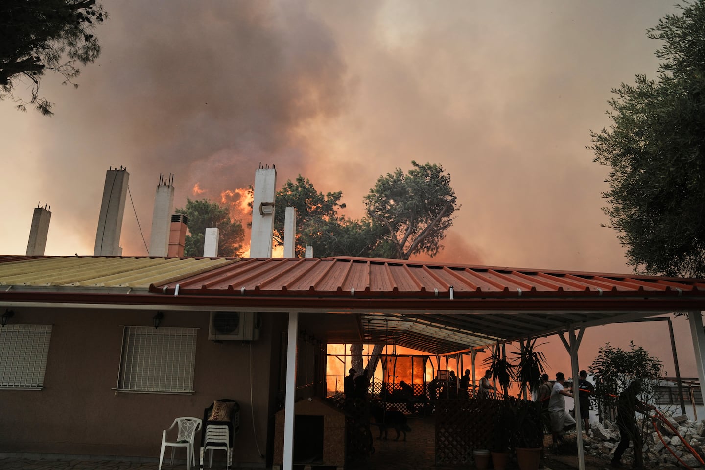 Firefighters and others try to control a wildfire approaching a house in Patras city, western Greece, Wednesday.