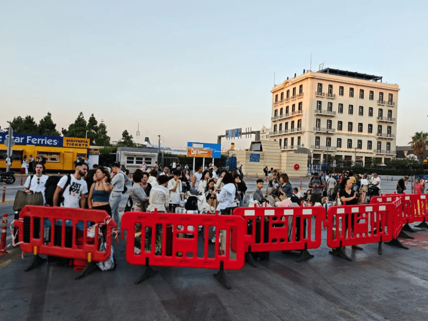 Crowds of people behind red barriers at a port.