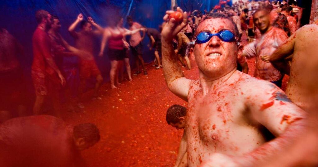 Man wearing swimming goggles throwing a tomato at La tomatina food fighting festival. Bunol. Valencia Spain
