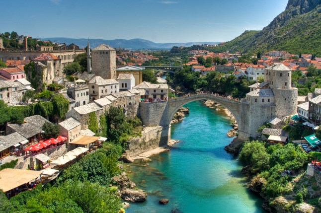 A bridge arching over the River Neretva in city of Mostar, Bosnia & Herzegovina, surrounded by buildings and greenery.