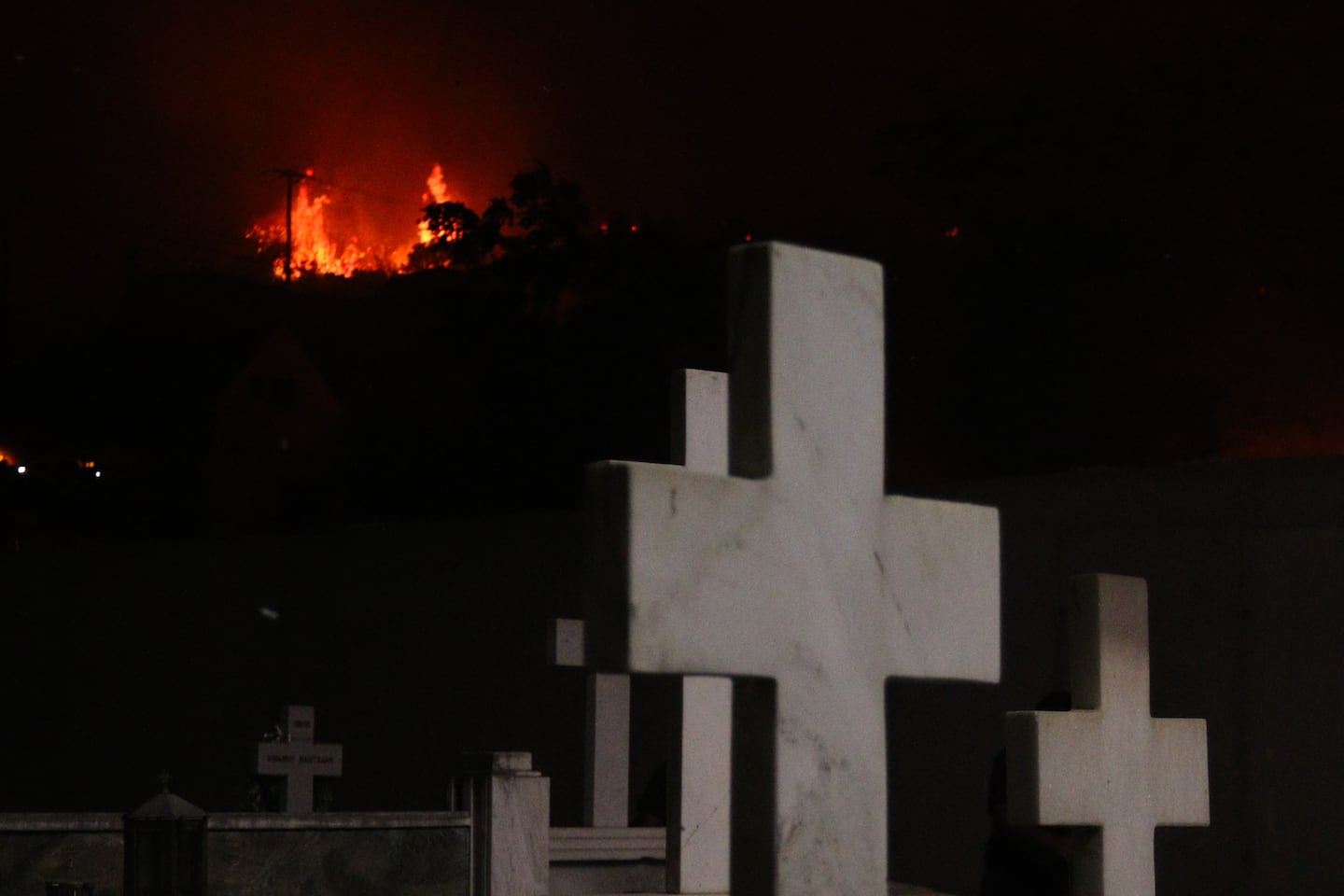 Wildfire burns behind a cemetery in Tsoukalaiika of Achaia, Peloponnese, Greece on Wednesday.