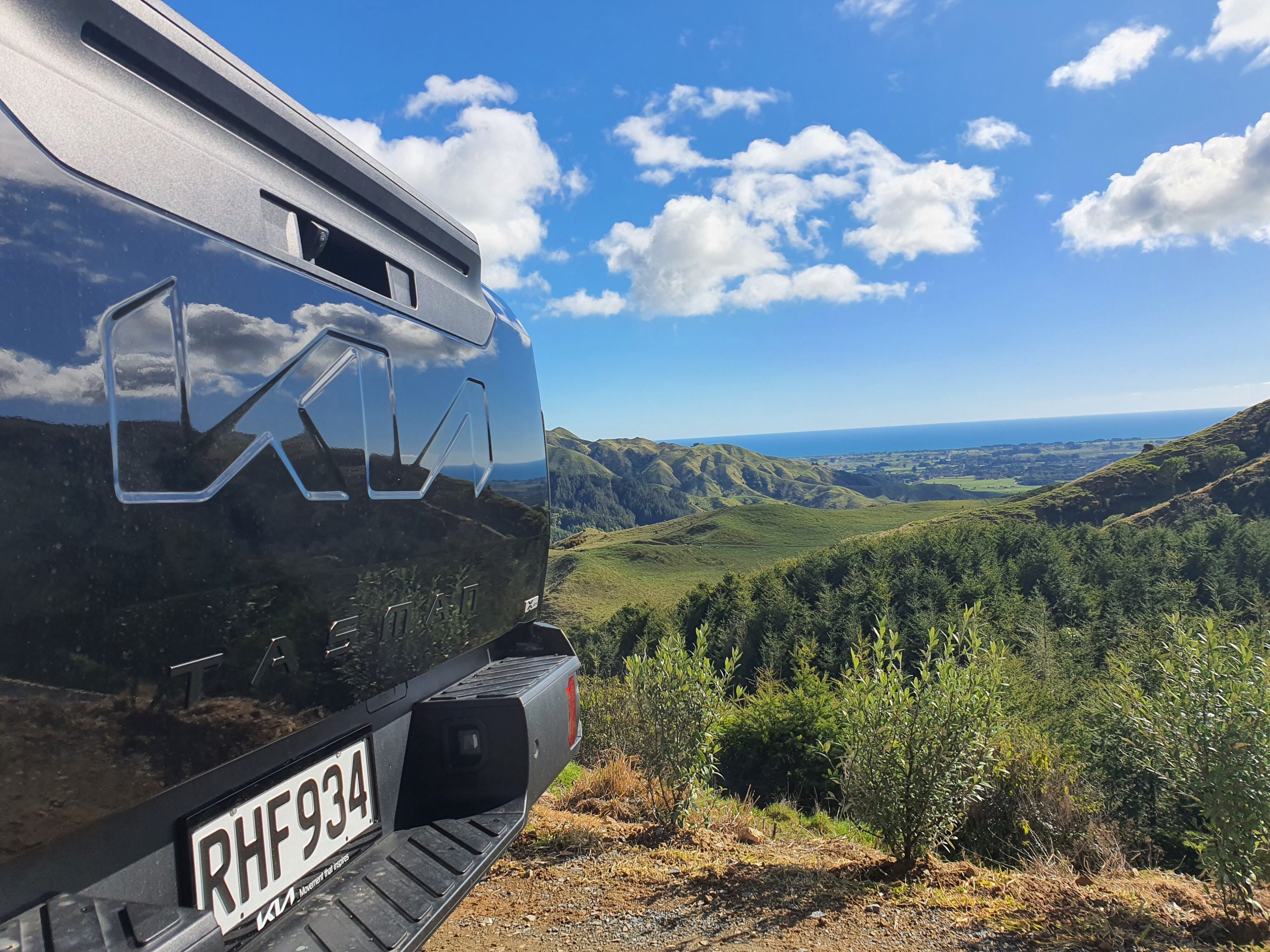 A photo of the Tasman Sea visible in the background, spotted past the rear of a Kia Tasman ute on the 2025 Kia Tasman launch at Dirt Farm, Te Horo, Hautere, just outside of Wellington.