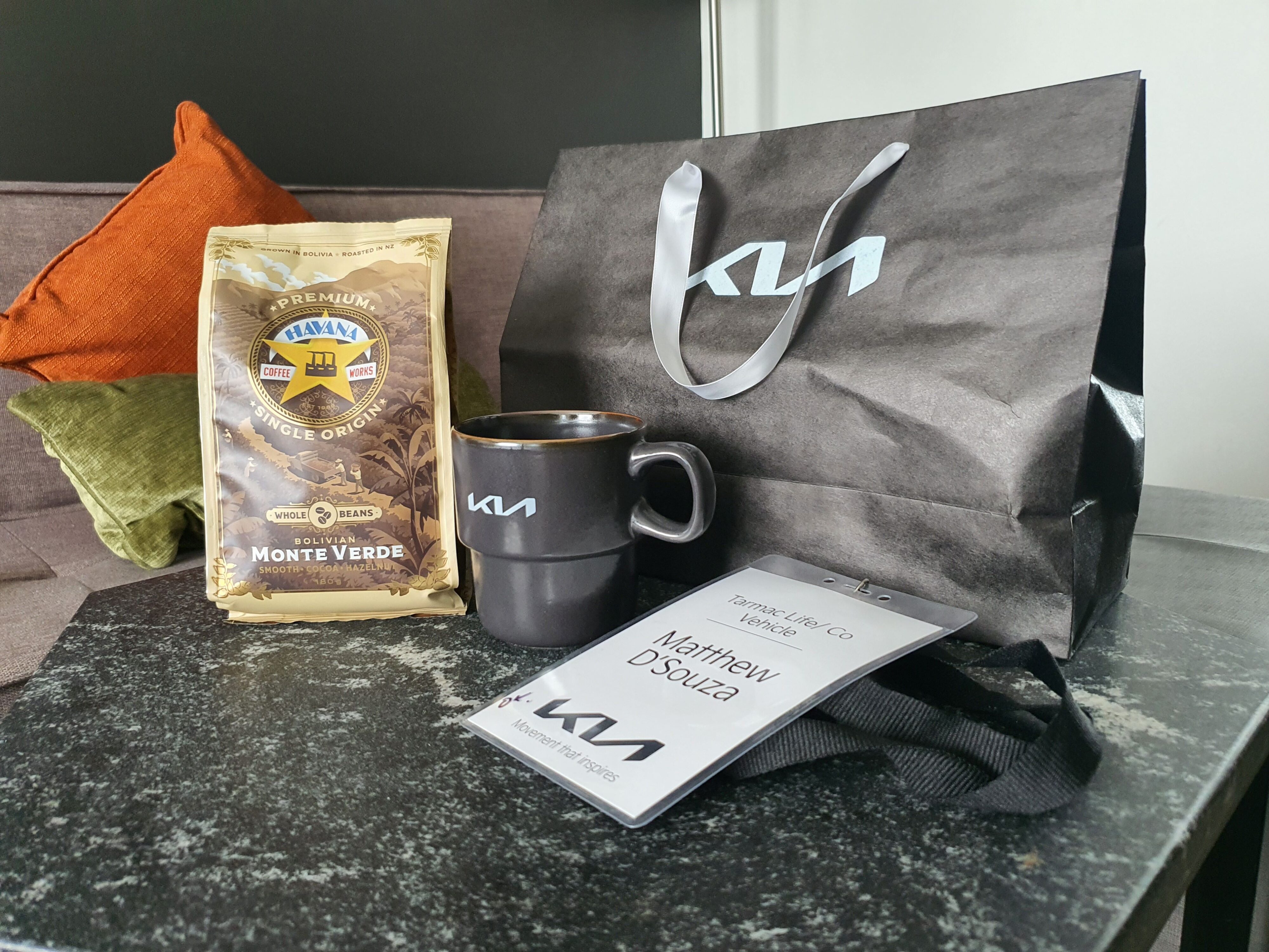 A photo of all of the goodies provided to us on the launch of the 2025 Kia Tasman. These include a bag of Havana coffee beans, two Kia branded stackable coffee cups and a name tag for Matthew D'Souza.