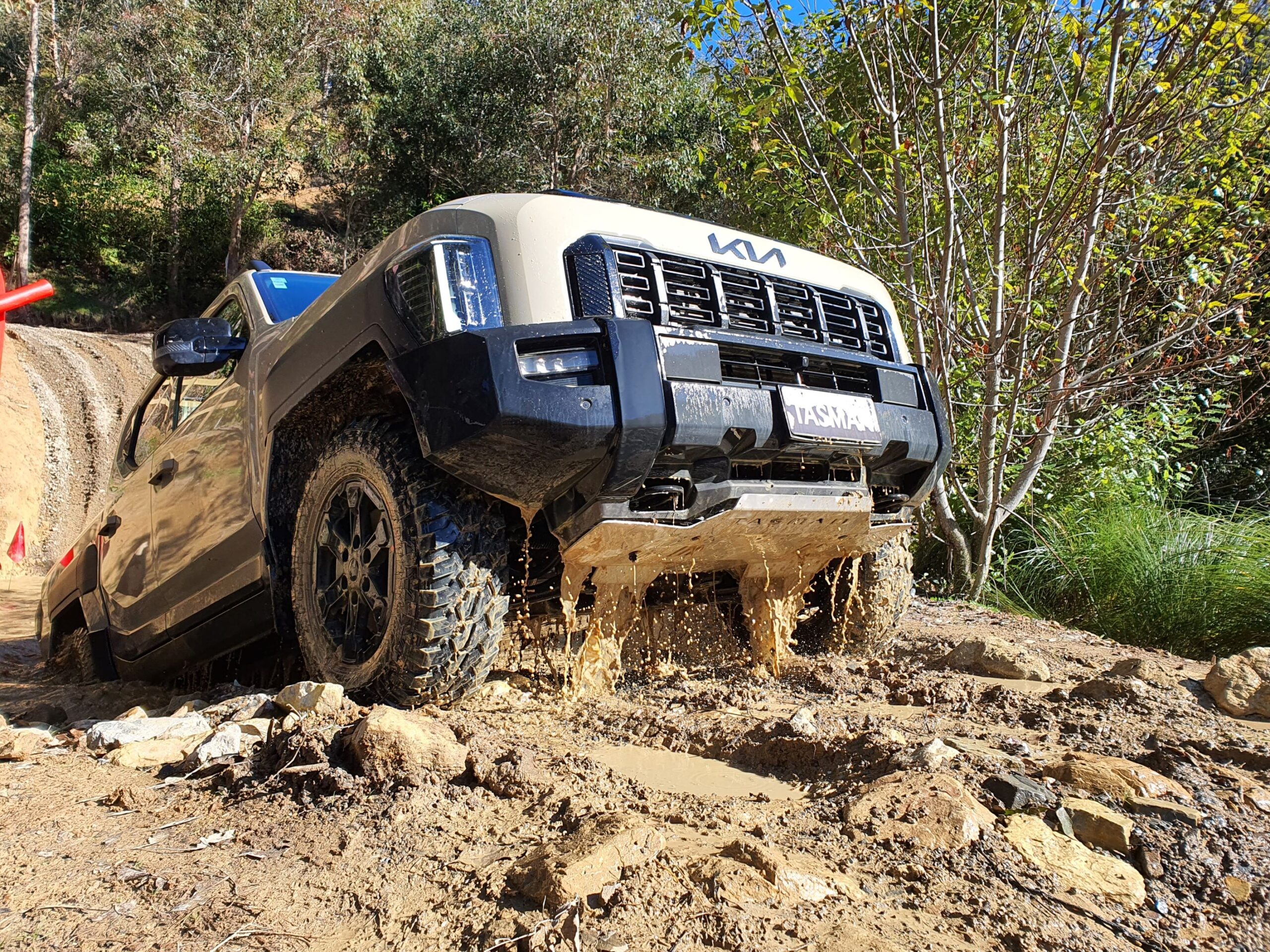 A photo of a Tan Beige coloured Kia Tasman ute emerging from a pool of water after completing the wading test on the 2025 Kia Tasman launch at Dirt Farm, Te Horo, Hautere, just outside of Wellington.