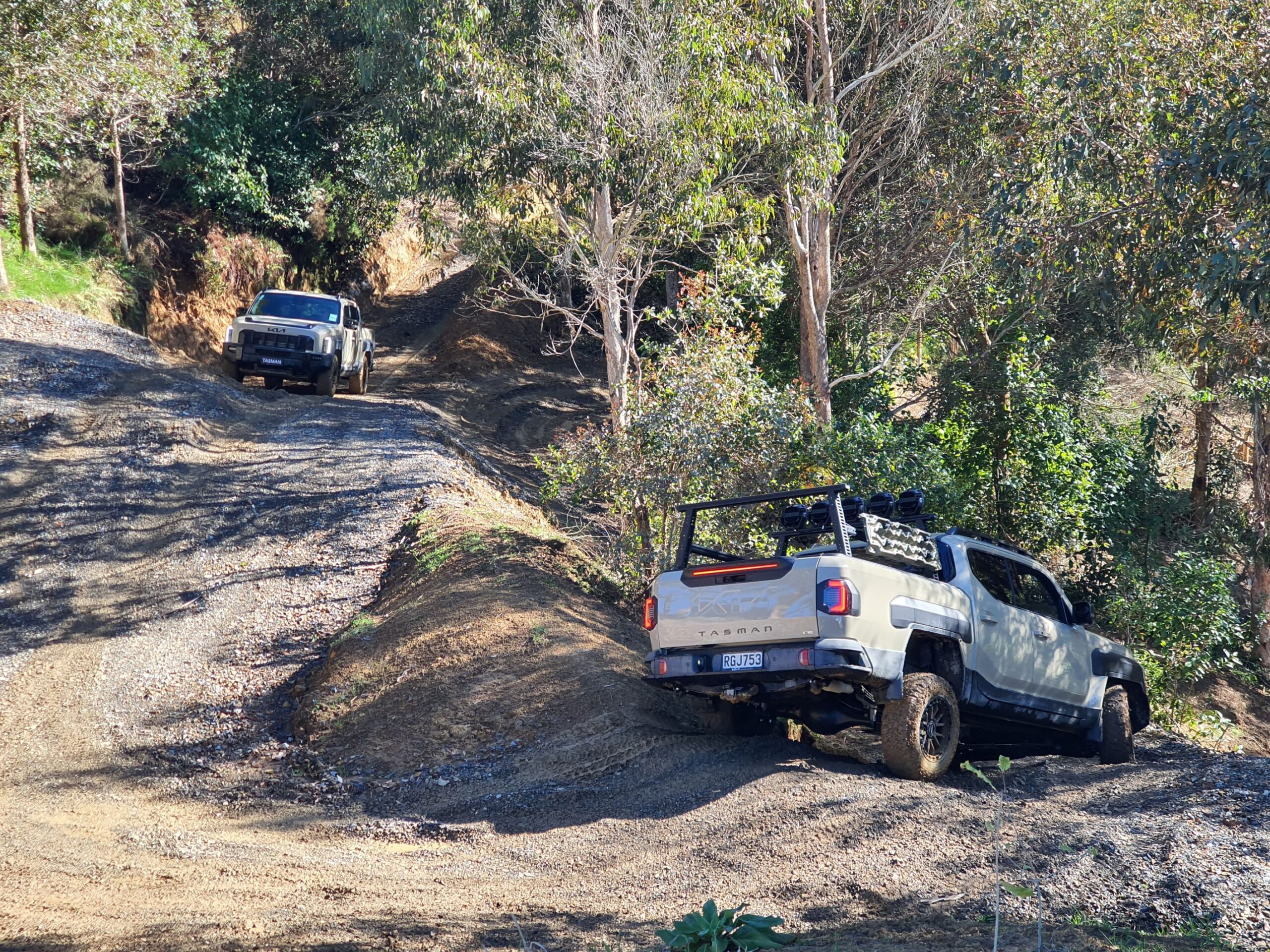 A photo of two Tan Beige coloured Kia Tasman utes tackling a series of steeply banked corners on the 2025 Kia Tasman launch at Dirt Farm, Te Horo, Hautere, just outside of Wellington.