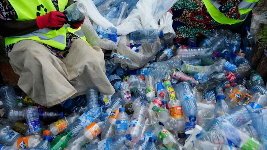 Workers use razor blades to scrape off labels from different soft-drink plastic bottles at the Street Waste Company in Lagos, Nigeria, Monday, Aug 11, 2025. (AP Photo/Sunday Alamba)