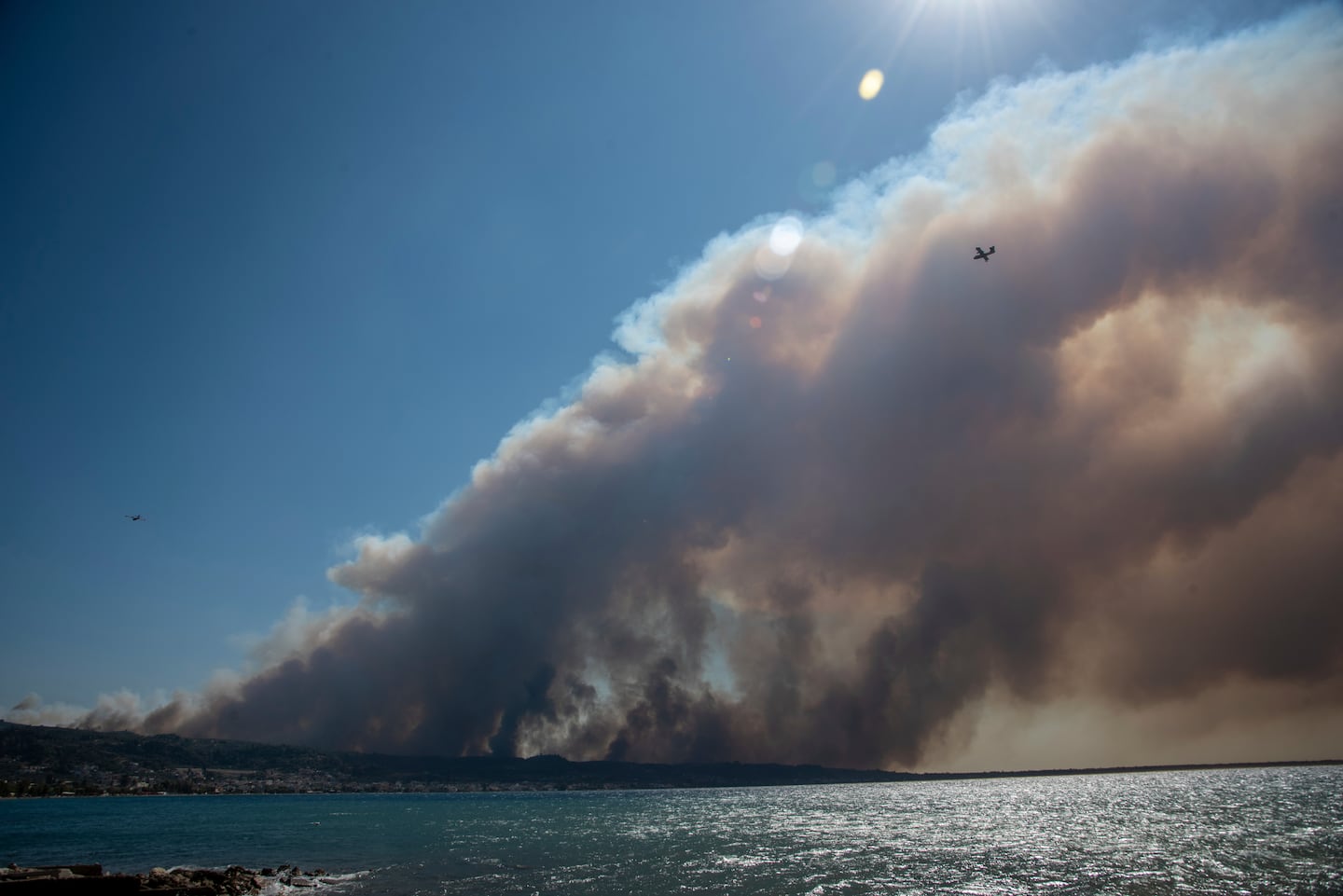 Smoke from a wildfire covers the sky as firefighting aircrafts fly over the village of Kato Achaia near Patras city, western Greece, Tuesday.