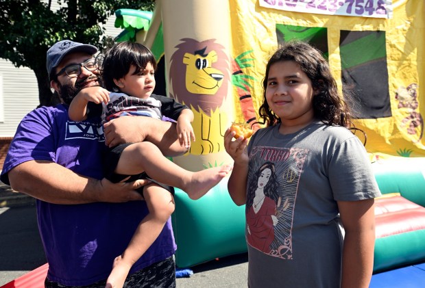 Eliel Alvarez of Reading holds 2-year0old Ezra, who is anxious to try out the bounce house, as his sister Emelia, 9, enjoys an orange during the Community Day at Penn Street sponsored by the Berks Community Health Center on Saturday, Aug. 9, 2025. (BILL UHRICH/READING EAGLE)