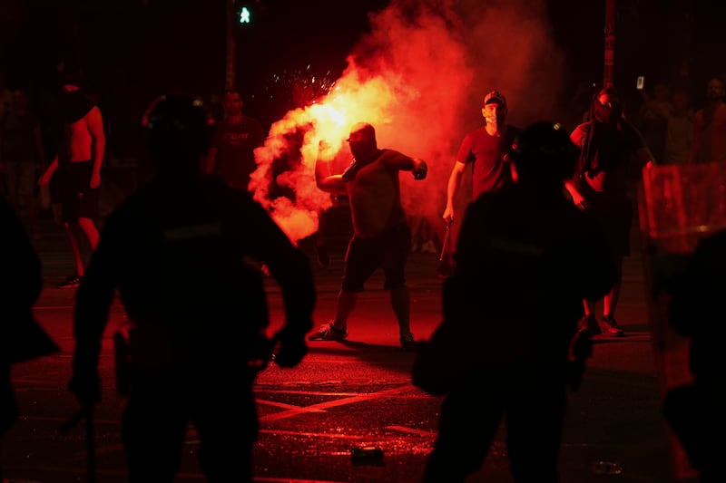 Supporters of Aleksandar Vucic hurl flares at anti-government protesters (Darko Vojinovic/AP)