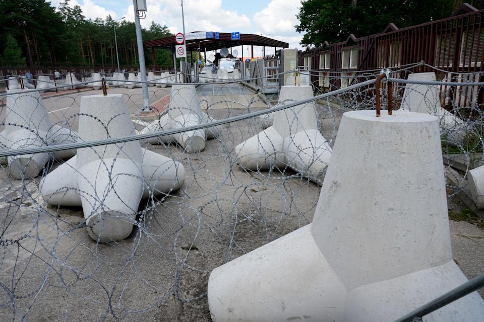 Large grey concrete tetrapods sit on the grey ground near a border crossing with barbed wire in front of them