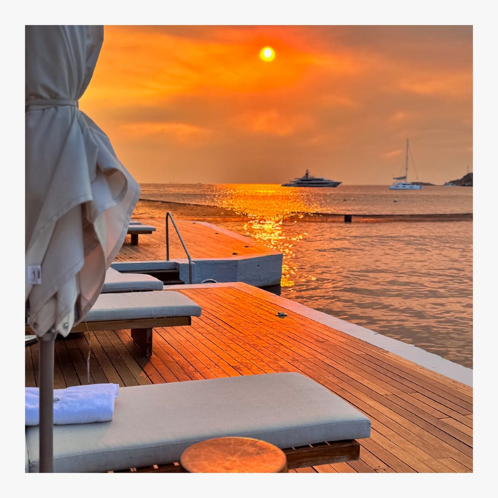 Serene beachside scene at sunset with loungers and boats.