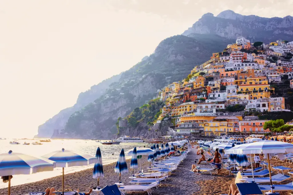 Italian beaches see sharp drop in visitors this summer View of Positano Beach on the Amalfi Coast, Italy, with rows of umbrellas and sunbeds along the shoreline and colorful hillside houses above the sea.