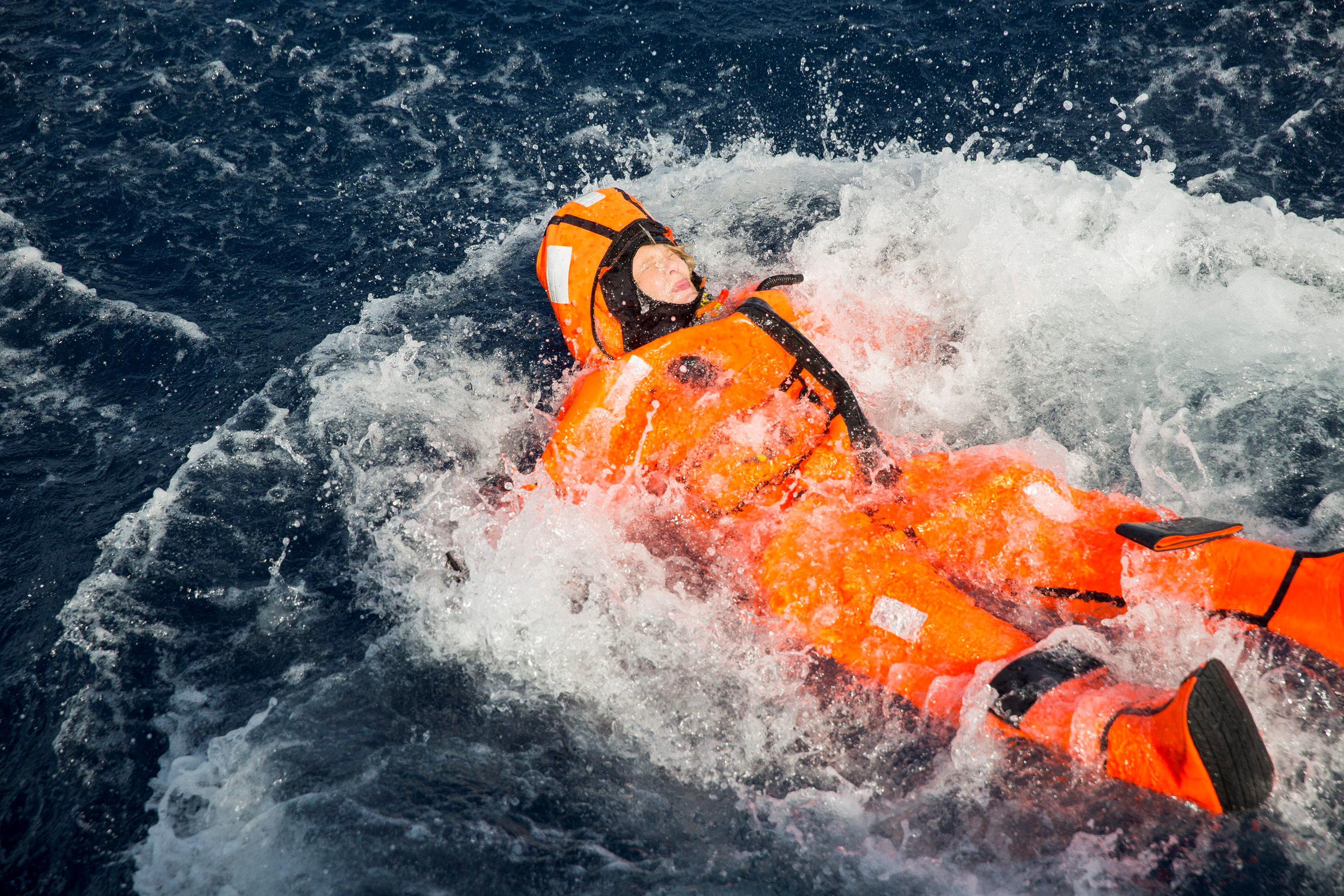 A person in an orange survival suit floats in the ocean.