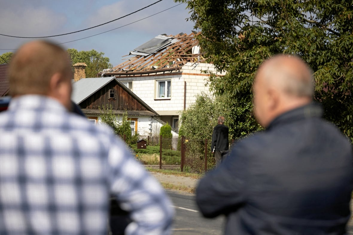 Two men look at a destroyed roof.
