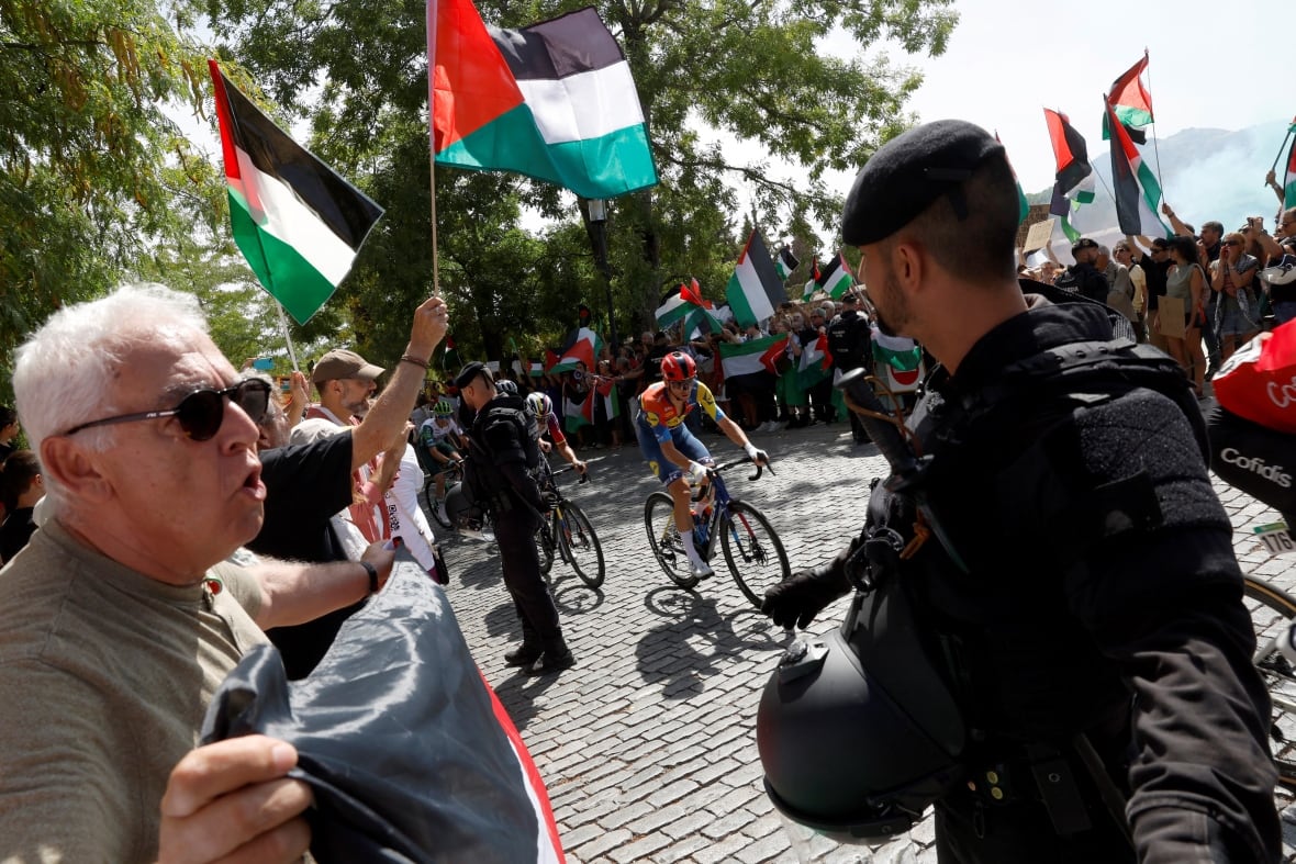 Police officers face off with protesters as cyclists race by.
