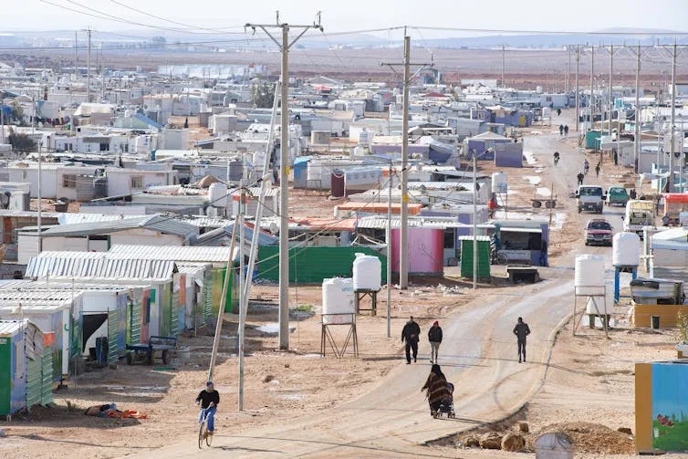 People and cars on a road running through a refugee camp in Jordan.