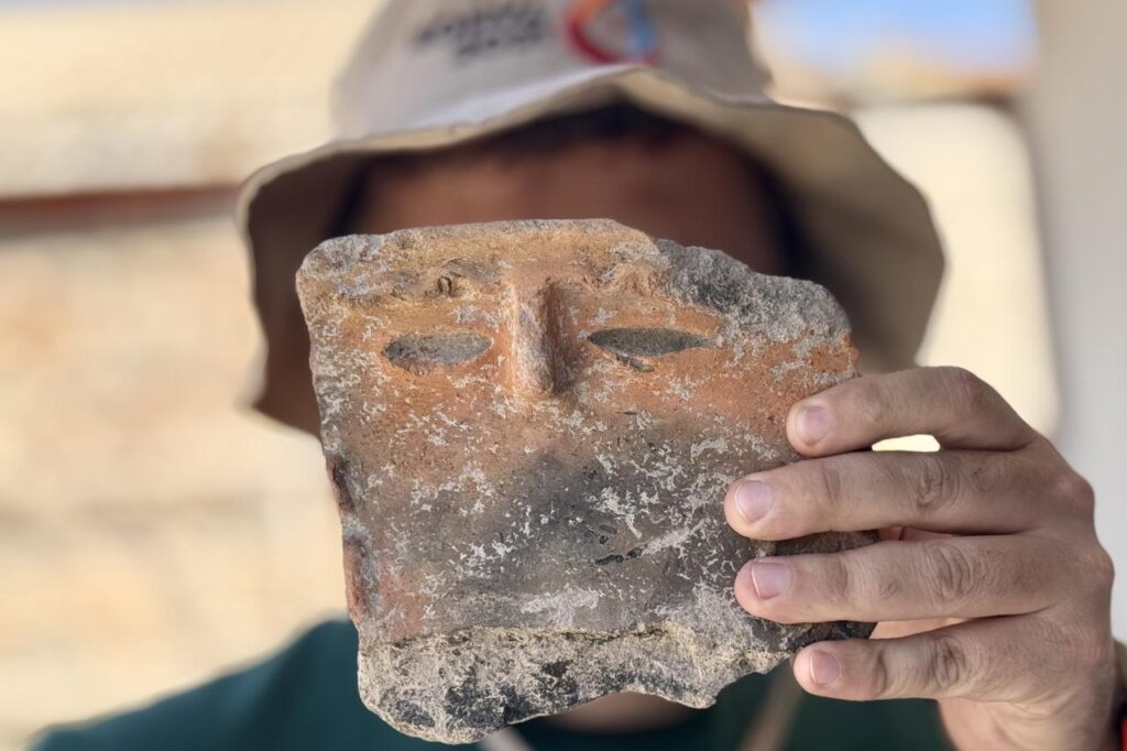An archaeologist displays a 5,000-year-old pottery fragment carved with a human face, unearthed during excavations at Gokhoyuk in Konya, Türkiye, Sept. 16, 2025. (AA Photo)