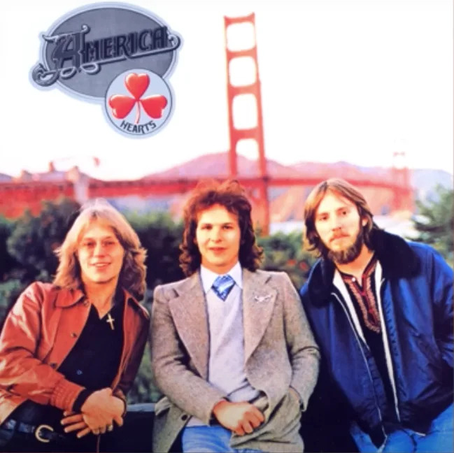 Three men from the band America pose in front of the Golden Gate Bridge. The album cover features the title "Hearts" with a clover emblem