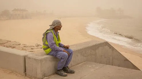 <span class="caption">A worker looking out to sea as a sandstorm hits Kuwait.</span> <span class="attribution"><a class="link " href="https://www.shutterstock.com/image-photo/kuwait-city-october-19-2023-migrant-2377481239" rel="nofollow noopener" target="_blank" data-ylk="slk:Sebastian Castelier / Shutterstock;elm:context_link;itc:0;sec:content-canvas">Sebastian Castelier / Shutterstock</a></span>