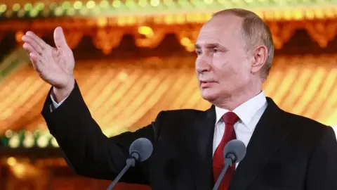 EPA Putin wearing a dark jacket, white shirt and red tie, extends his right hand in front of a podium with two microphones as he answers questions from journalists in Beijing