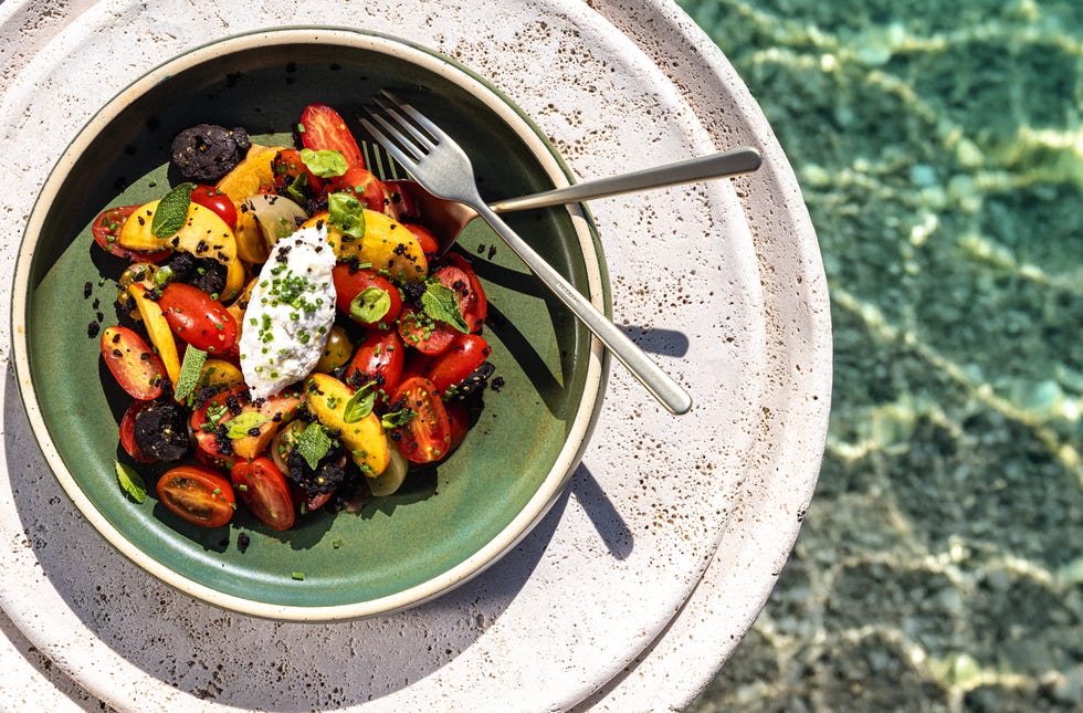 A vibrant salad with tomatoes, herbs, and cheese served in a green bowl.