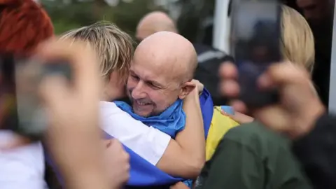 Ombudsman's Office The moment Dmytro Khyliuk was freed. The photo shows Dmytro hugging someone, while draped in a Ukrainian flag, with a big grin on his face