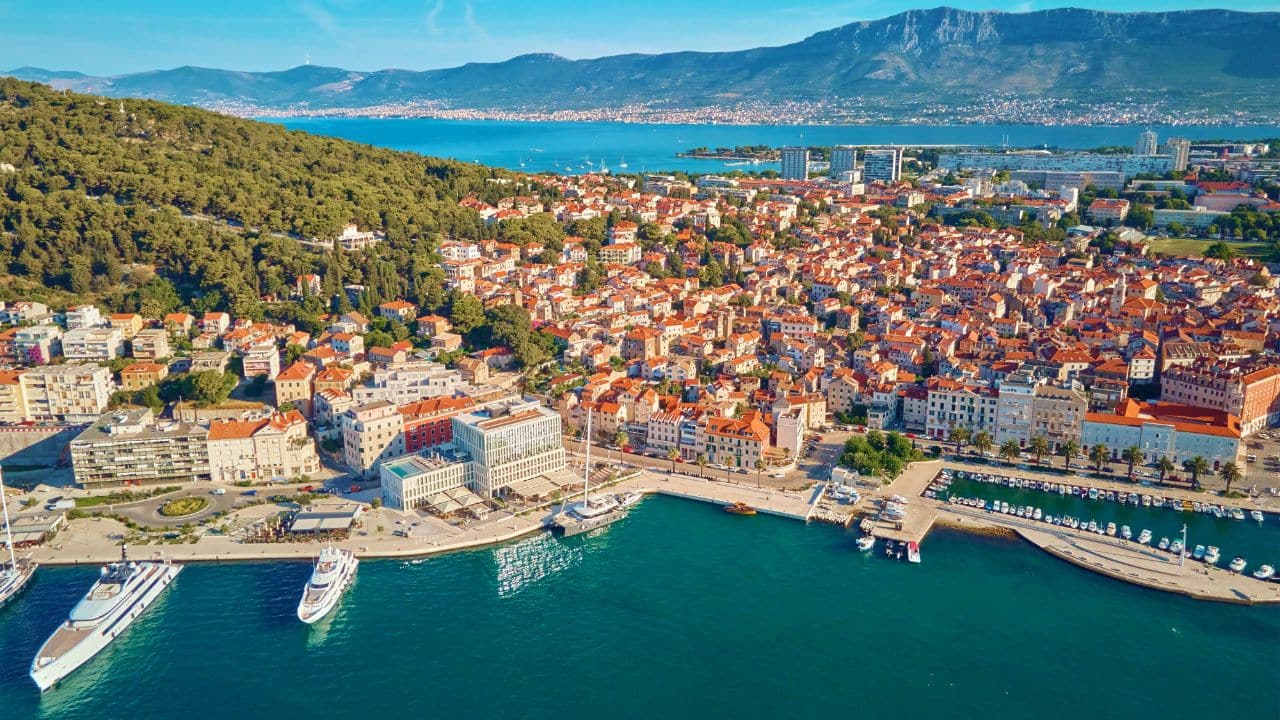 Aerial view of Split, Croatia. Cityscape of coastal touristic city with harbor with mountains in background. Old town with historical red roof tiled buildings near Adriatic Sea