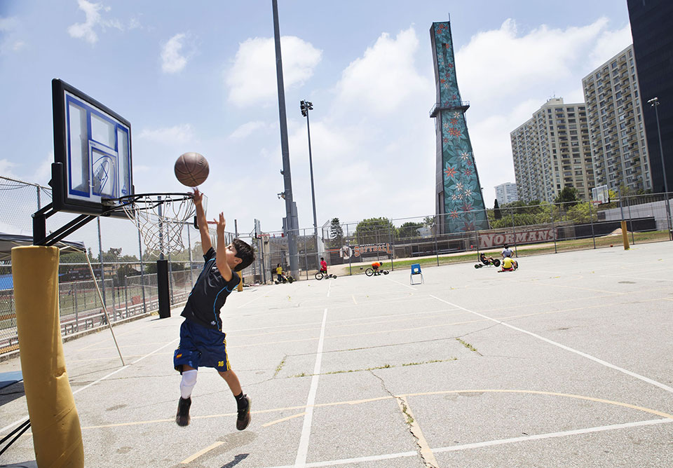 a young person plays basketball, oil drilling tower in the background