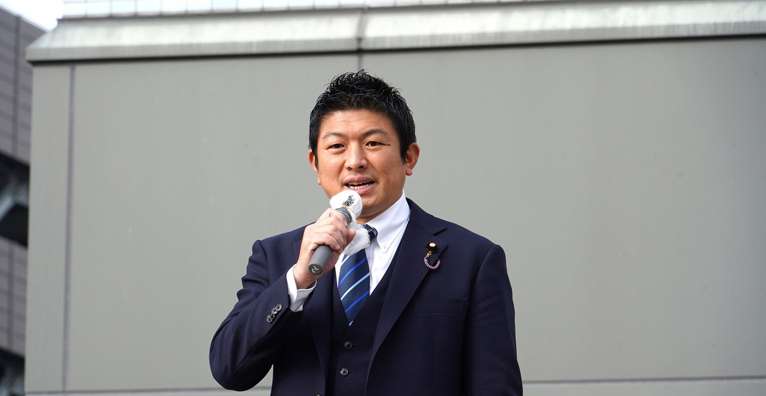 is it becoming more ‘European’? Sohei Kamiya wearing a dark blue suit and tie talking into a microphone.