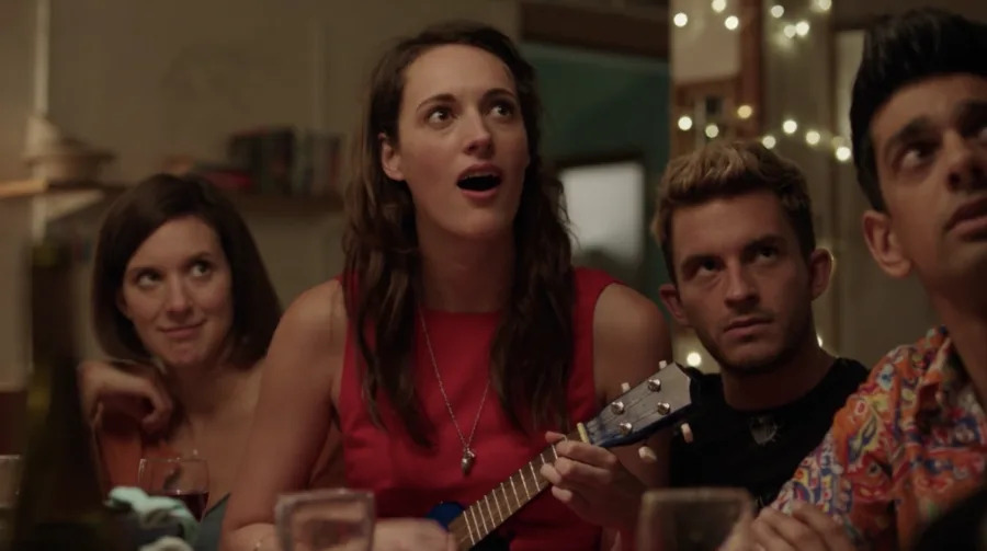 Group of four friends sitting at a table, with one person holding a ukulele, looking surprised and engaged