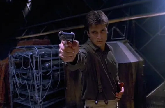 A person wearing a shirt and suspenders points a gun with a serious expression inside an industrial-looking setting