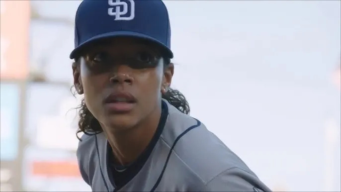 Person in baseball uniform with cap, focused on the field, appearing in an action scene possibly from a film or TV show
