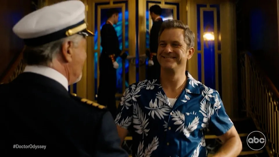 Man in tropical shirt smiling, talking to a ship's captain, with two crew members in the background holding white towels