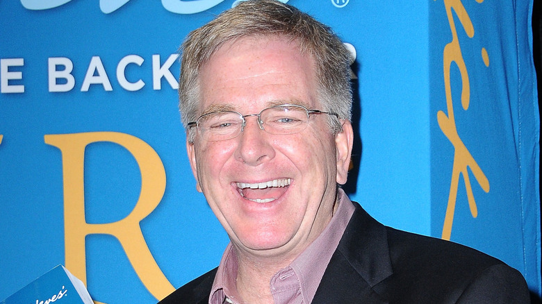 Rick Steves smiles in glasses and a black blazer