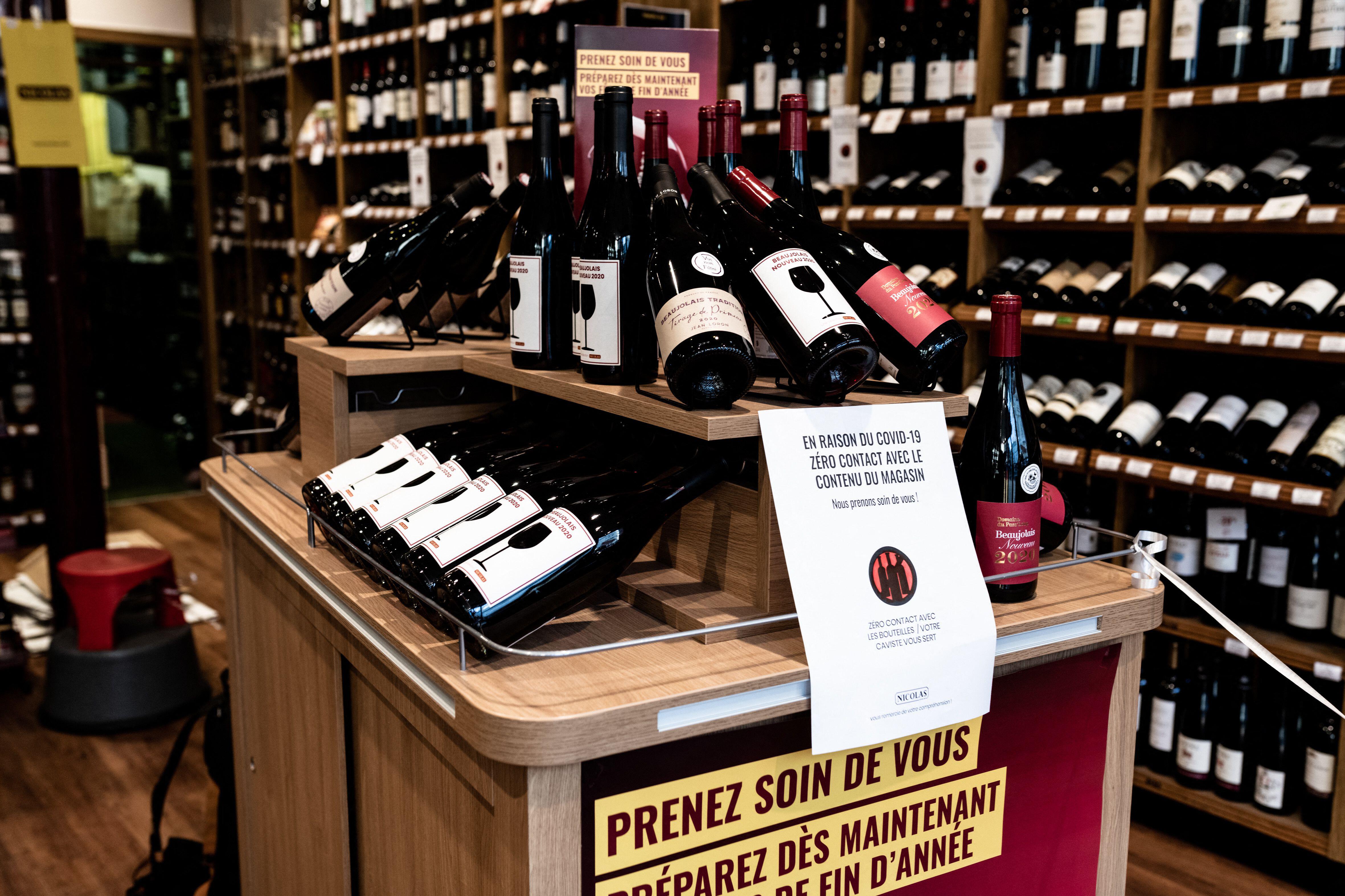 Bottles of Beaujolais Nouveau wine on display for sale in a Nicolas wine shop with COVID-19 signage.