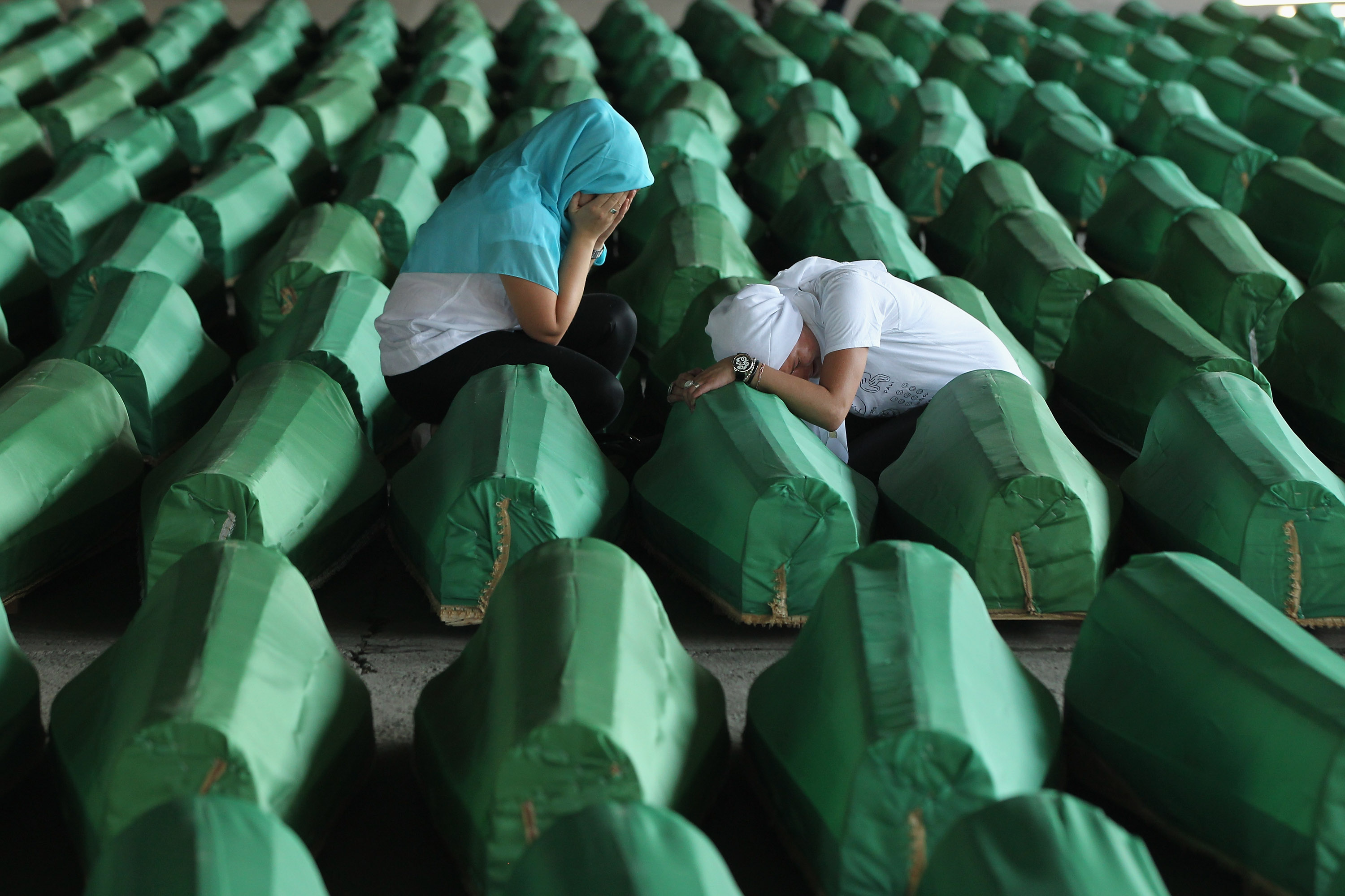 Two Muslim women crying over coffins of Srebrenica massacre victims.