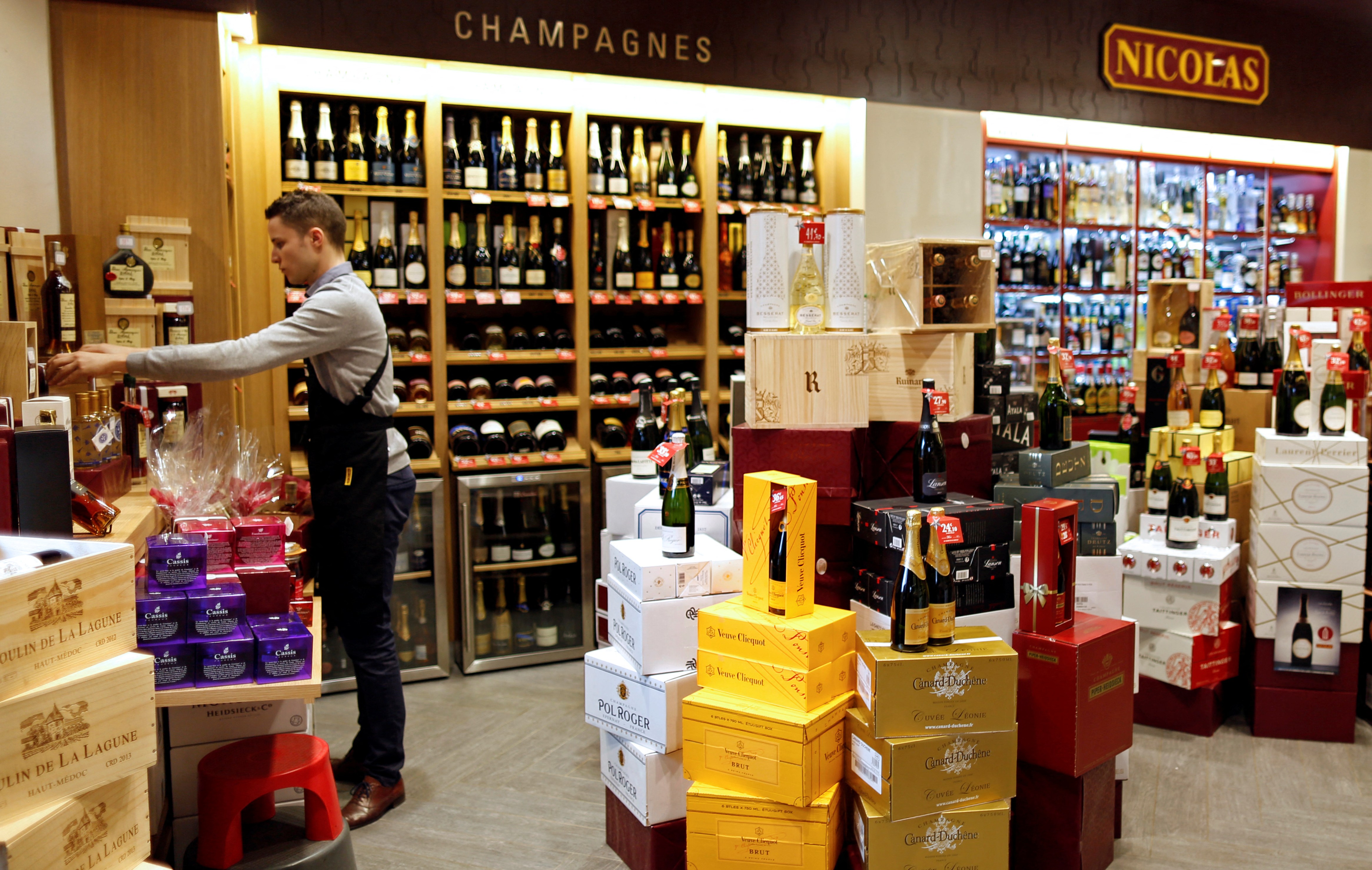 A man works in a Nicolas French wine specialist store where bottles of champagne are displayed.