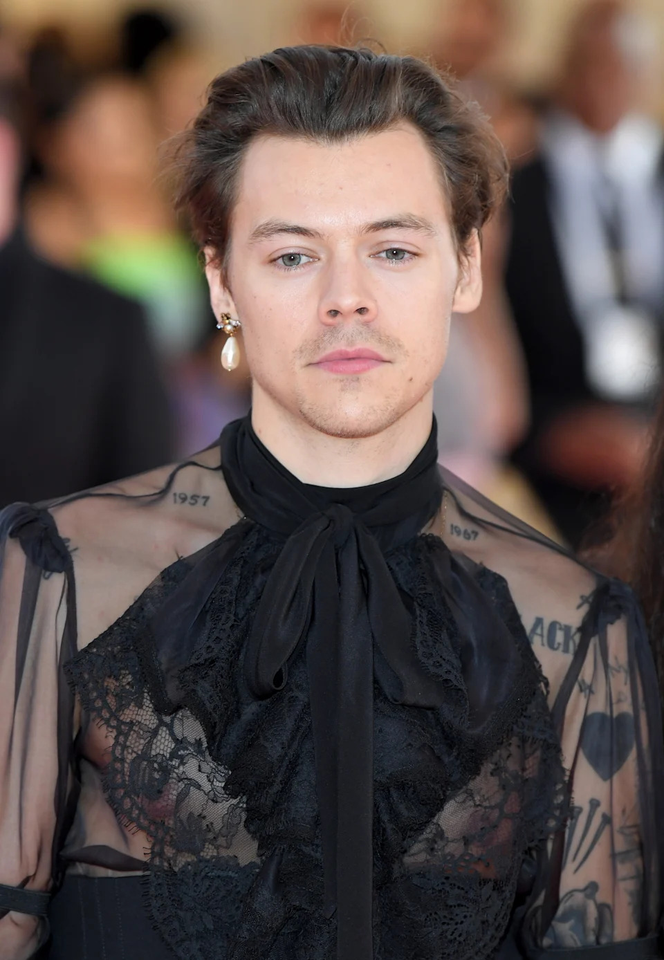 Harry Styles is wearing a sheer lace top and large pearl earring at the 2019 Met Gala