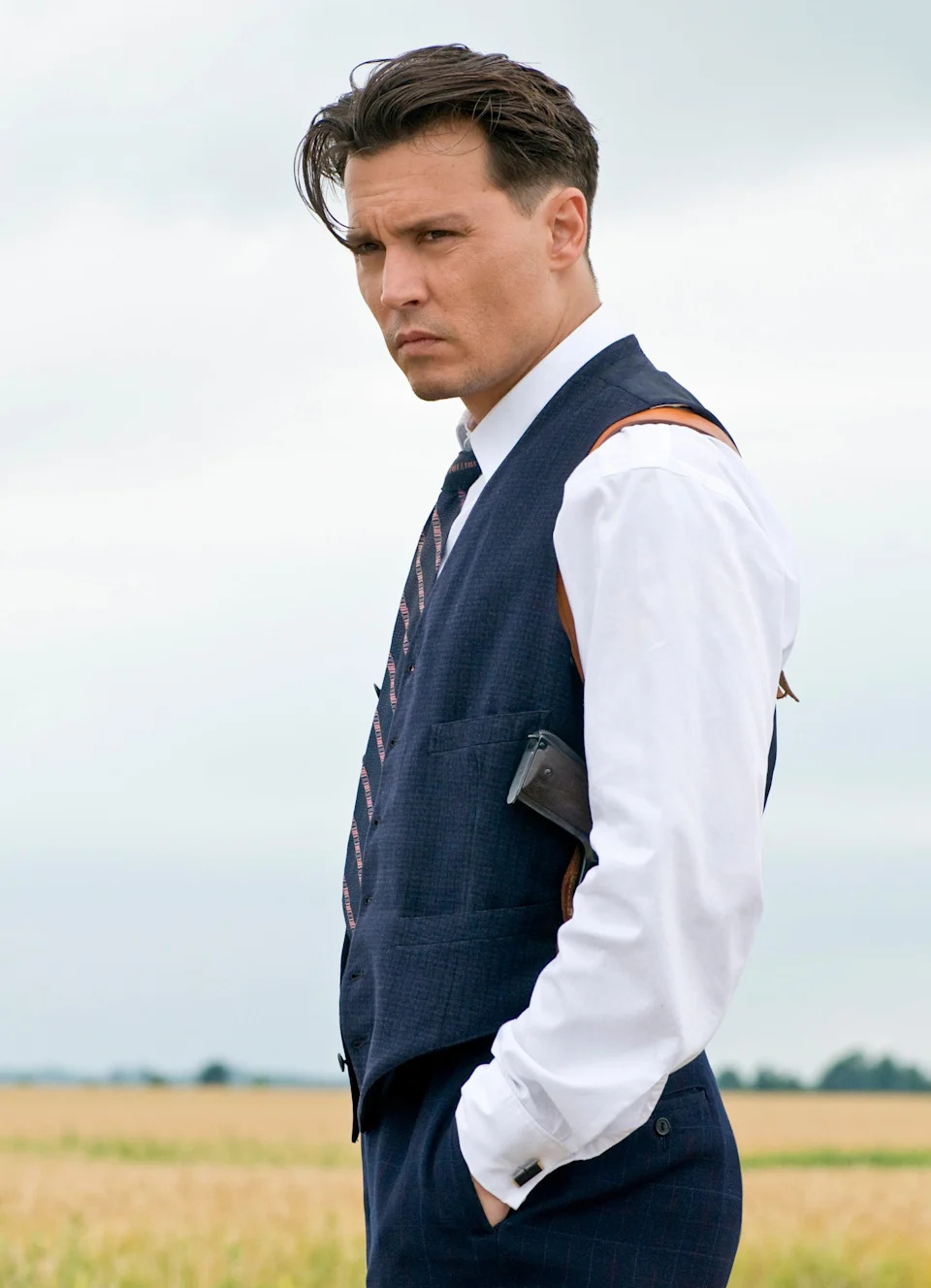 Johnny Depp is wearing a vest, tie, pants, and button-up shirt while he stands in a field