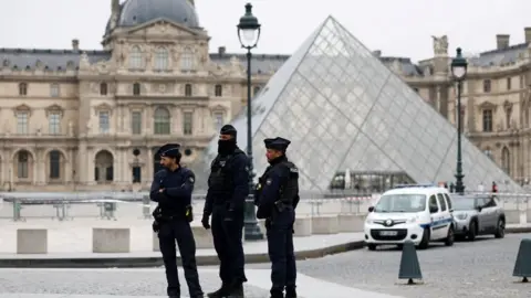Reuters Three police officers stand outside the Louvre's famous glass pyramid entrance