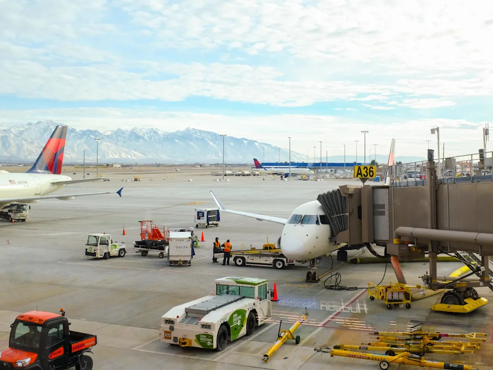 A Delta plane is parked at a gate with mountains in the background