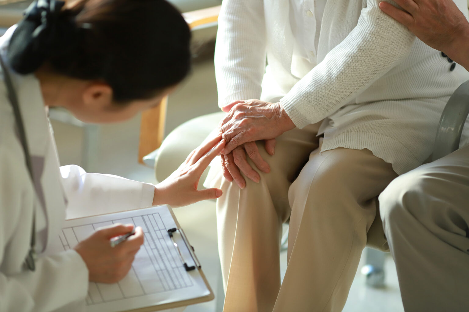 A young doctor checks her elderly patient's knee.