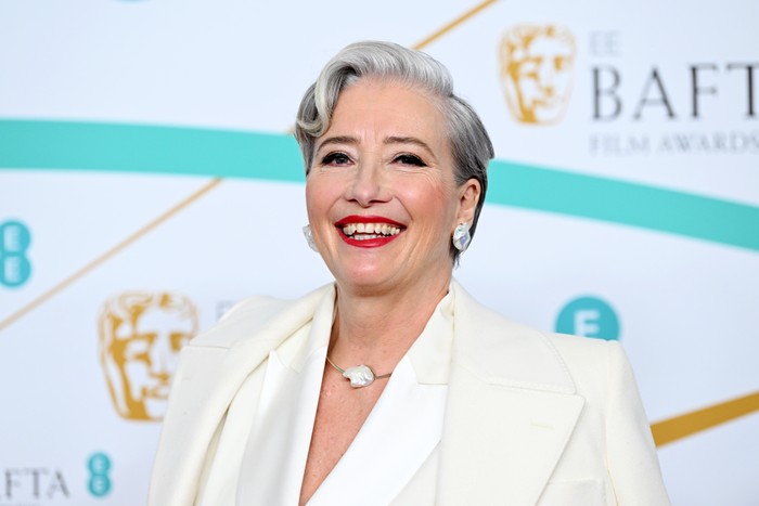 EE BAFTA Film Awards 2023 – Red Carpet Arrivals Emma Thompson smiling ahead in front of a white BAFTA background. She is wearing an all-white suit.