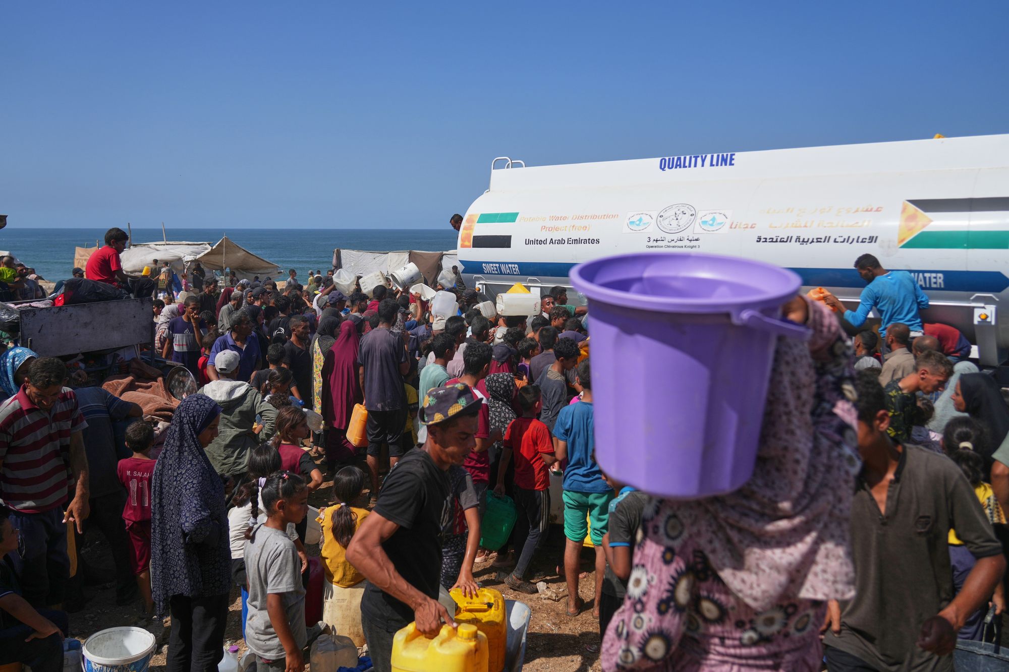 Displaced Palestinians gather to collect water from a truck at a makeshift camp in Nuseirat, central Gaza Strip