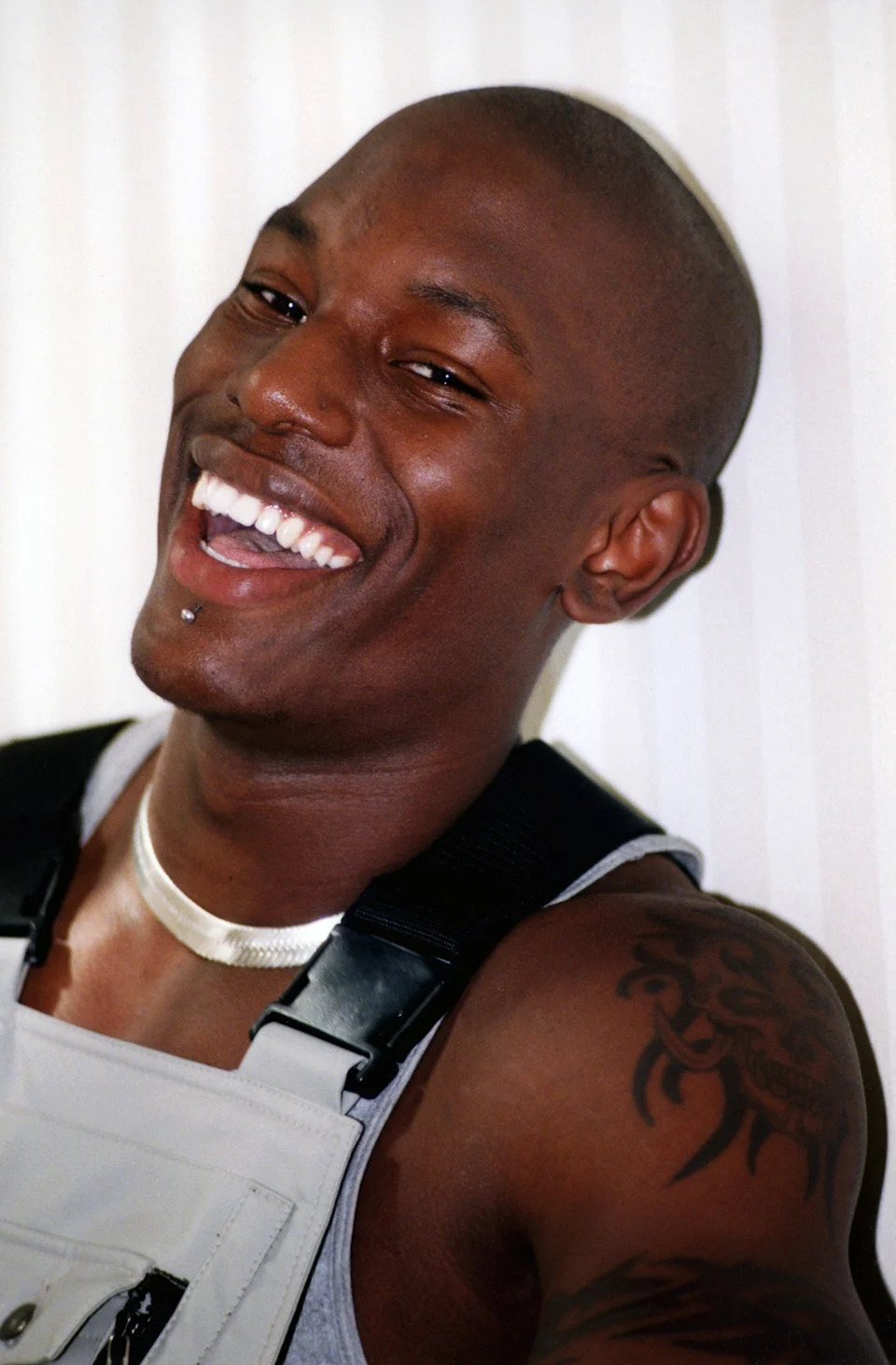 Tyrese Gibson is wearing overalls, a silver necklace, and has a lip piercing in 1998. His shoulder tattoo is exposed