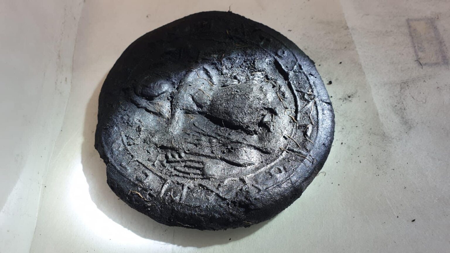 Carbonized round loaf showing a raised figure and surrounding Greek letters