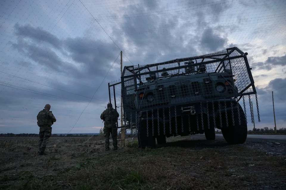 Ukrainian soldiers stand before an armoured military vehicle surrounded by a cage to protect against drone attacks on a road near Oleksandrivka (AFP via Getty Images)